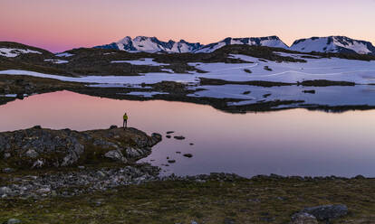 Person standing by lake in mountains - JOHF06916