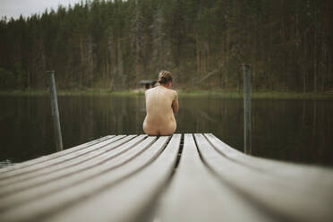 Naked woman sitting on jetty - JOHF06953