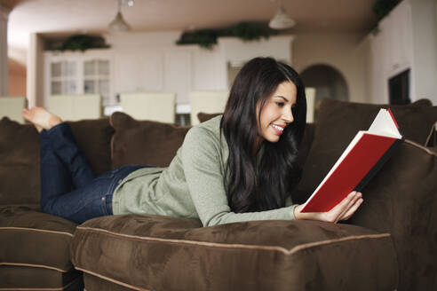 Frau liest ein Buch auf ihrer Couch zu Hause - CAVF73859