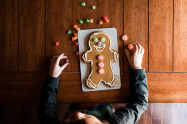 Kleines Kind beim Verzieren eines Lebkuchenmännchens auf dem Küchentisch - CAVF73871