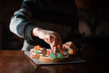 Kleine Hände berühren einen Kaugummi auf einem Lebkuchenmann-Keks auf dem Tisch - CAVF73872