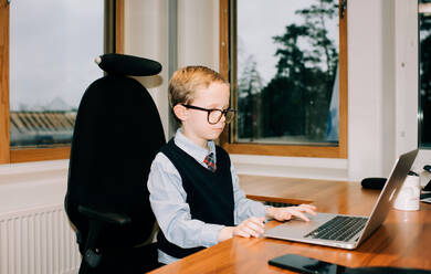 Young boy working in his dads office working on a computer - CAVF73932