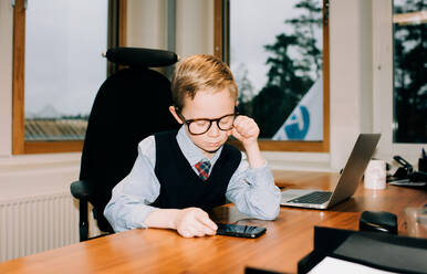 Young boy working in an office looking at his dads phone at work - CAVF73935