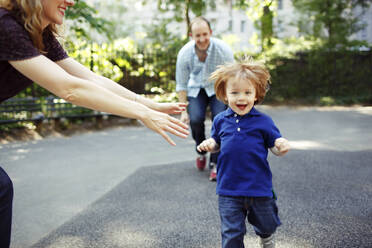 Boy running towards camera as parents playfully chase him - CAVF74040