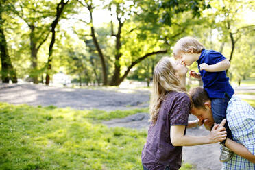 Vater hält Sohn auf den Schultern im Park mit Mutter gibt Sohn Kuss - CAVF74052