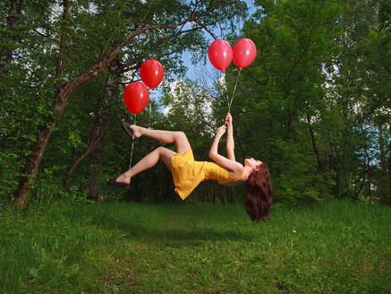 Adorable young brunette girl levitating on balloons in a park - CAVF74270