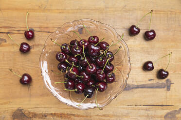 Cherries in glass bowl on wooden table - GWF06412