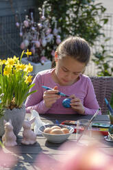 Konzentriertes Mädchen sitzt am Gartentisch und bemalt Ostereier - LBF02860