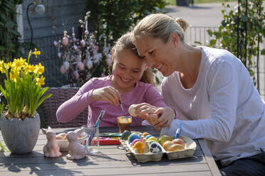 Glückliche Mutter und Tochter sitzen am Gartentisch und bemalen Ostereier - LBF02861