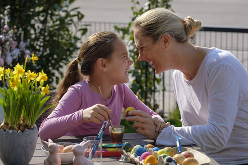Glückliche Mutter und Tochter bemalen Ostereier am Gartentisch und haben Spaß dabei - LBF02862