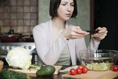 Porträt einer Frau, die mit ihrem Smartphone einen Salat fotografiert - EYAF00912