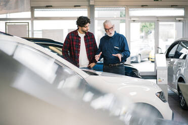 Car dealer showing car to young man in showroom - MOEF02727