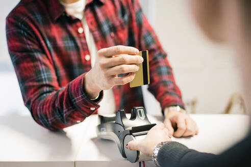 Nahaufnahme eines Mannes, der mit einer Kreditkarte an der Kasse eines Geschäfts bezahlt - MOEF02744