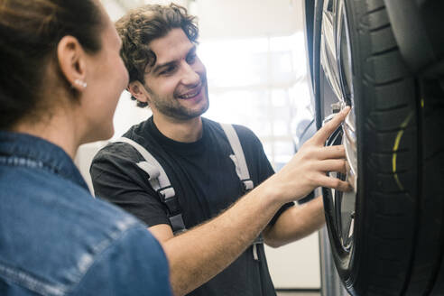 Ein lächelnder Automechaniker und ein Kunde betrachten einen Reifen in der Werkstatt - MOEF02749