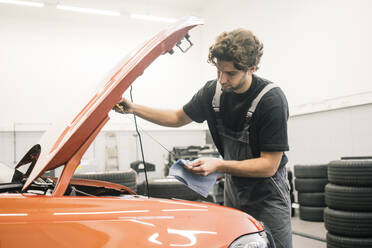 Automechaniker in einer Werkstatt bei der Arbeit am Auto, der den Ölmessstab überprüft - MOEF02753