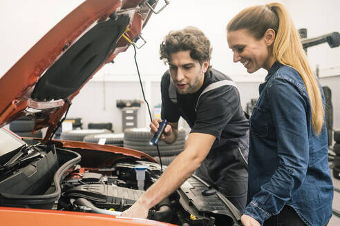 Automechaniker im Gespräch mit einem Kunden in der Werkstatt - MOEF02754