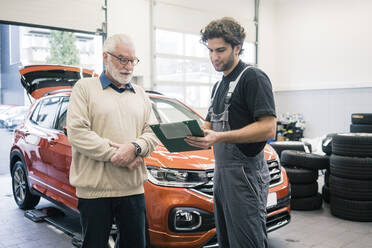 Car mechanic explaining ckeck list to client in workshop - MOEF02773