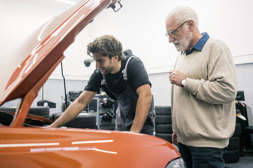 Automechaniker im Gespräch mit einem Kunden in der Werkstatt - MOEF02775