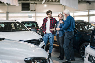 Car dealer showing cars to couple in showroom - MOEF02776