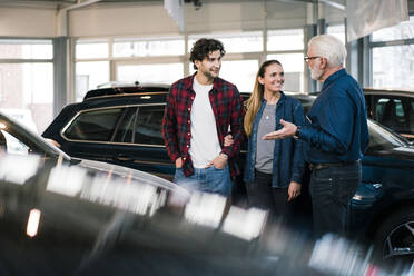 Autohändler zeigt einem Paar Autos im Ausstellungsraum - MOEF02778