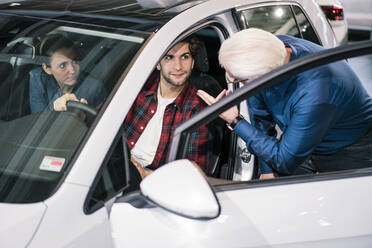 Car dealer showing car to couple in showroom - MOEF02780