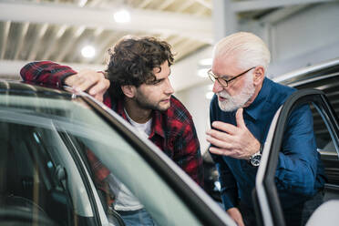 Car dealer showing car to young man in showroom - MOEF02781