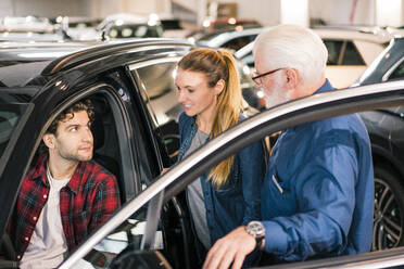 Car dealer showing car to couple in showroom - MOEF02783