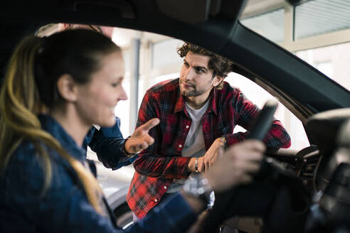 Autohändler zeigt einem Paar ein Auto im Ausstellungsraum - MOEF02784