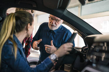 Car dealer showing car to couple in showroom - MOEF02785