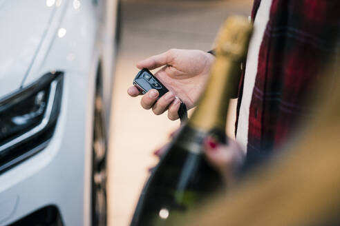 Nahaufnahme eines Paares mit Schlüssel und Sektflasche an einem neuen Auto - MOEF02787