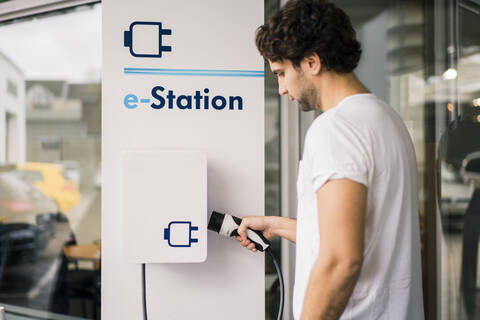 Mann beim Aufladen eines Elektroautos an einer Tankstelle, lizenzfreies Stockfoto