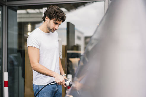 Mann beim Aufladen eines Elektroautos an einer Tankstelle - MOEF02795