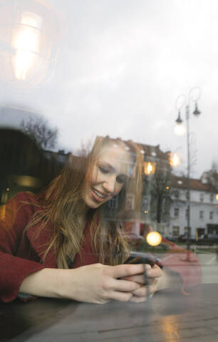 Porträt einer lächelnden jungen Frau, die in einem Café ein Mobiltelefon benutzt, lizenzfreies Stockfoto