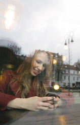 Porträt einer lächelnden jungen Frau, die in einem Café ein Mobiltelefon benutzt - AHSF01848
