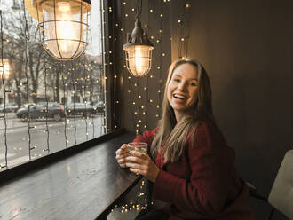 Portrait of laughing young woman with cup of tea in a coffee shop - AHSF01849