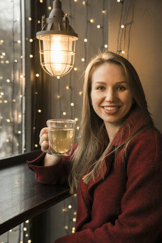 Porträt einer lächelnden jungen Frau mit einem Glas Tee in einem Kaffeehaus, lizenzfreies Stockfoto