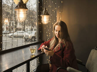 Junge Frau mit einer Tasse Tee in einem Café sitzend und mit einem Mobiltelefon telefonierend - AHSF01852