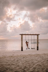 Woman on a swing at the sea at sunset, Maguhdhuvaa Island, Gaafu Dhaalu Atoll, Maldives - DAWF01226