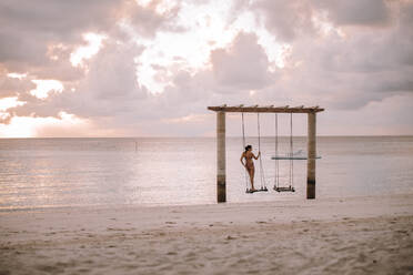 Frau auf einer Schaukel am Meer bei Sonnenuntergang, Insel Maguhdhuvaa, Gaafu Dhaalu Atoll, Malediven - DAWF01227