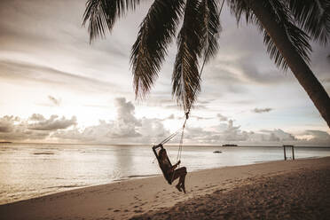 Frau auf einer Schaukel am Meer bei Sonnenuntergang, Insel Maguhdhuvaa, Gaafu Dhaalu Atoll, Malediven - DAWF01231