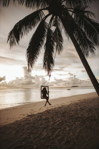 Woman on a swing at the sea at sunset, Maguhdhuvaa Island, Gaafu Dhaalu Atoll, Maldives stock photo