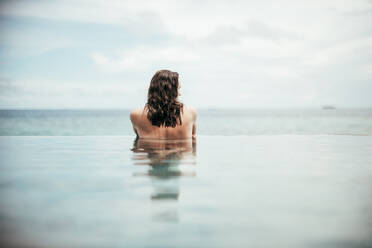 Rear view of woman relaxing in infinity pool, Maguhdhuvaa Island, Gaafu Dhaalu Atoll, Maldives - DAWF01243