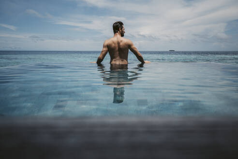 Rückansicht eines Mannes, der im Infinity-Pool entspannt, Insel Maguhdhuvaa, Gaafu Dhaalu Atoll, Malediven - DAWF01247