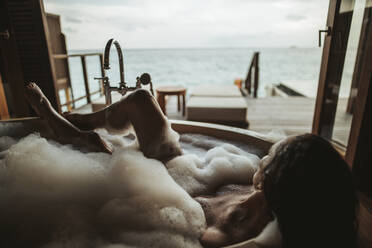 Frau entspannt sich in der Badewanne mit Blick auf das Meer, Insel Maguhdhuvaa, Gaafu Dhaalu Atoll, Malediven - DAWF01254