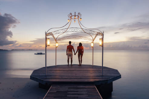 Pärchen auf Steg am Meer bei Sonnenuntergang, Insel Maguhdhuvaa, Gaafu Dhaalu Atoll, Malediven - DAWF01256
