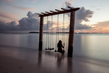 Frau auf einer Schaukel am Meer bei Sonnenuntergang, Insel Maguhdhuvaa, Gaafu Dhaalu Atoll, Malediven - DAWF01257