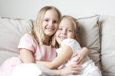 Portrait of two little girls hugging each other on the couch - EYAF00917