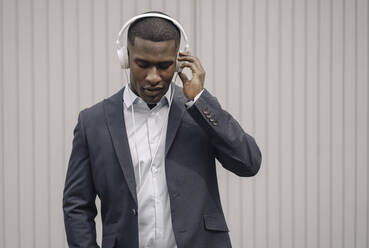 Porträt eines jungen Geschäftsmannes mit geschlossenen Augen, der mit Kopfhörern im Freien Musik hört - KNSF07404