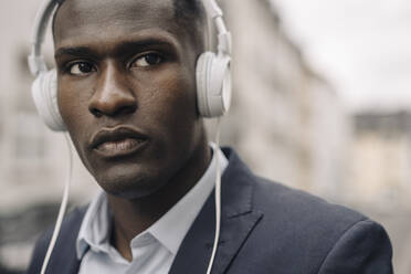 Portrait of young businessman wearing white headphones - KNSF07406
