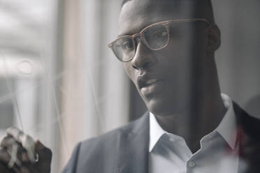 Portrait of young businessman drawing on glass pane in office - KNSF07411